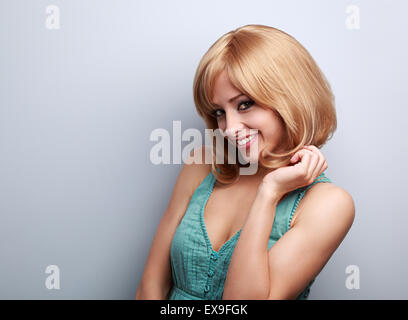 Schöne kokette junge Frau mit blonden kurzen Haarstil suchen mit Lächeln auf blauem Hintergrund Stockfoto