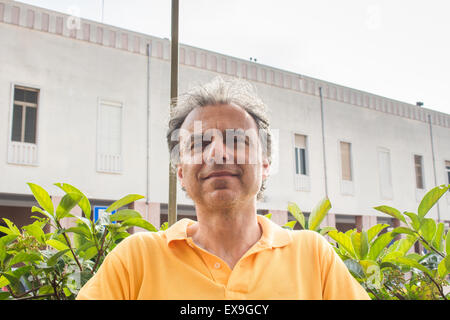 Nahaufnahme von hübsch stilvoll im mittleren Alter Sport Mann mit drei-Tage-Bart und Salz Cand Pfeffer Haar trägt ein gelbes Polo Shirt mit alten Gebäude im Hintergrund Stockfoto