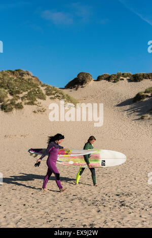 Zwei Surfer tragen ihre Surfbretter auf Crantock Beach in Newquay, Cornwall. Stockfoto