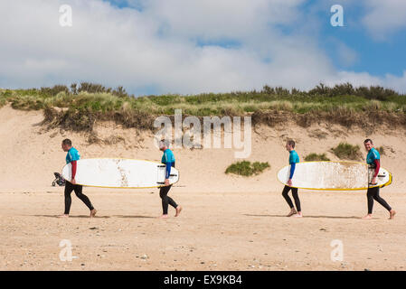 Surfer tragen ihre Surfbretter auf Fistral Beach in Newquay, Cornwall. Stockfoto