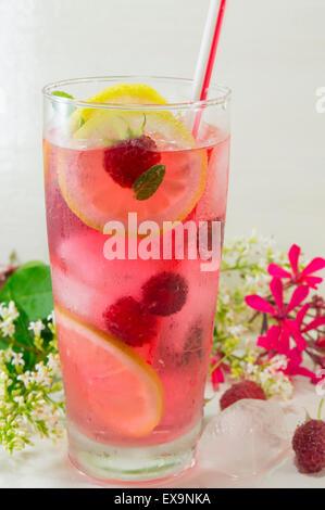 Hausgemachten Himbeer-Eistee mit Zitrone Himbeere und Eiswürfeln auf einem Tisch mit Blumen geschmückt Stockfoto