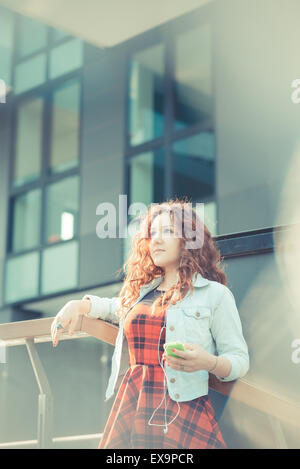 junge schöne Hipster Frau mit roten Locken Musik hören in der Stadt Stockfoto
