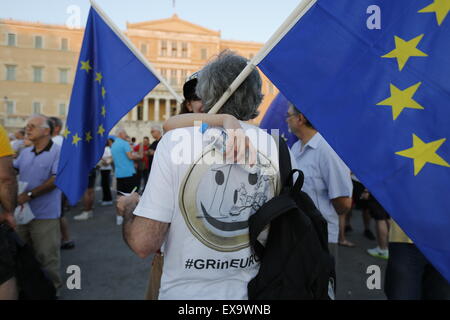 Athen, Griechenland. 9. Juli 2015. Ein Demonstrant trägt ein T-shirt mit einem Lächeln auf den Lippen Euro und und liest "#GRinEURO" bei der pro-Europa-Protest in Athen. Er trägt eine Europaflagge. Tausende von Griechen protestierten vor dem griechischen Parlament gegen einen möglichen Grexit. Man nennt sie die griechische Regierung um sicherzustellen, dass Griechenland in Europa und in der Eurozone bleiben wird. Stockfoto