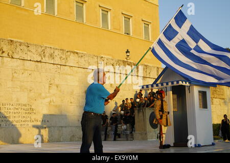 Athen, Griechenland. 9. Juli 2015. Ein Demonstrant Wellen eine große griechische Flagge vor dem griechischen Parlament, griechische Bereitschaftspolizei und eine Evzone (Präsidentengarde) kann im Hintergrund gesehen werden. Tausende von Griechen protestierten vor dem griechischen Parlament gegen einen möglichen Grexit. Man nennt sie die griechische Regierung um sicherzustellen, dass Griechenland in Europa und in der Eurozone bleiben wird. Bildnachweis: Michael Debets/Pacific Press/Alamy Live-Nachrichten Stockfoto