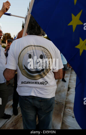 Ein Demonstrant trägt ein T-shirt mit einem Lächeln auf den Lippen Euro und und liest "#GRinEURO" bei der pro-Europa-Protest in Athen. Er trägt eine Europaflagge. Tausende von Griechen protestierten vor dem griechischen Parlament gegen einen möglichen Grexit. Man nennt sie die griechische Regierung um sicherzustellen, dass Griechenland in Europa und in der Eurozone bleiben wird. Stockfoto