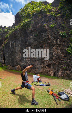 Ein Kletterer dehnt sich aus, während er sich vor dem Gesicht eines Kalksteinhügels für ein Sportklettern in Gunungkidul, Indonesien, vorbereitet. Stockfoto