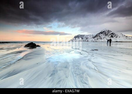 Sonnenuntergang und Wanderer am Skagsanden Strand umgeben von Schnee bedeckt Berge, Flakstad, Lofoten-Inseln, Arktis, Norwegen Stockfoto