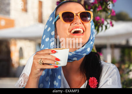 Glückliche Frau trinken Kaffee In einem Café im Freien, in den Sonnenuntergang. Vintage-Stil, Fokus auf Tasse Kaffee. Geringe Schärfentiefe Stockfoto