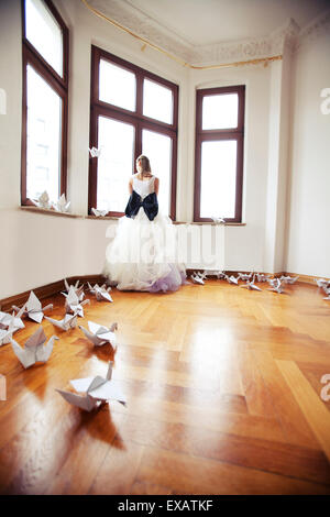 Braut in einer leeren Wohnung in einem alten Gebäude steht, schaut aus dem Fenster Stockfoto