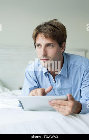 Mann im Bett mit digital-Tablette, wegschauen mit kontemplativen Blick Stockfoto