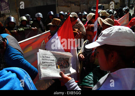 La Paz, Bolivien, 10. Juli 2015. Ein Protestteilnehmer aus Potosi liest während eines Protests des Gesellschaftskomitees und der Anhänger von Potosi eine Zeitung. Sie sind in La Paz, um von der Regierung die Einhaltung der Wahlversprechen zu fordern, die sie der Region in der Vergangenheit gegeben hat. In der Schlagzeile steht, dass 3 Minen und öffentliche Gebäude in Potosi als Teil der Proteste besetzt werden. Die roten und weißen Flaggen sind die Flaggen des Departements Potosí. Kredit: James Brunker / Alamy Live News Stockfoto