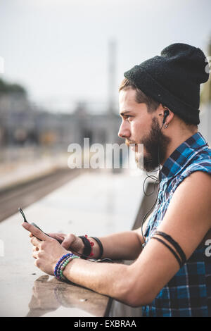 hübscher Junge bärtige Hipster Mann mit Smartphone und hören Musik mit Kopfhörern in der Stadt