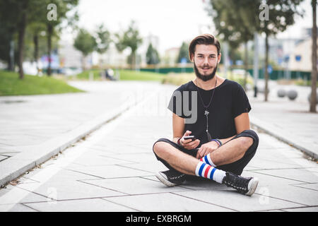 hübscher Junge bärtige Hipster Mann mit Smartphone und hören Musik mit Kopfhörern in der Stadt Stockfoto