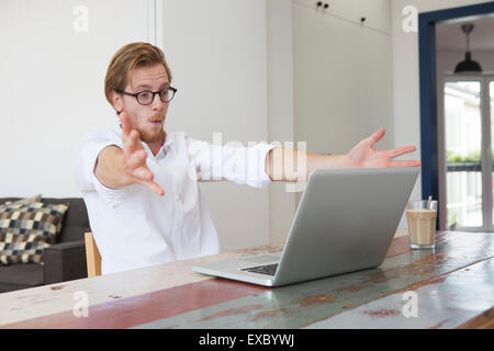 Rothaarige junger Mann mit seinem Laptop am Tisch sitzen und auf der Suche nach betont und aufgeregt Stockfoto