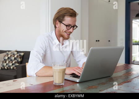 rothaarige junge Mann arbeitet an seinem Laptop und lächelt Stockfoto