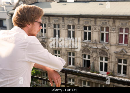 rothaarige junge Mann stehend auf Balkon und Blick auf einem alten Mietshaus Stockfoto