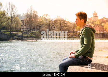 3/4 Länge des kontemplativen Licht braun behaarte Teenager tragen grüne Kapuzen-Shirt und Jeans Jeans sitzen auf Wand Stockfoto