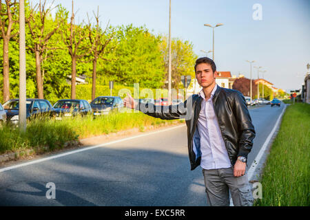 Hübscher junger Mann, ein Tramper warten Auto am Straßenrand in der Stadt, tragen schwarze Lederjacke Stockfoto