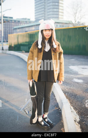 junge schöne asiatische Hipster-Frau in der Stadt - mit lustigen Schweinchen Wintermütze Stockfoto