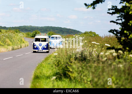 Zwei alte klassische VW-Wohnmobile aus den 60er Jahren fahren im Konvoi durch die englische Sommerlandschaft Stockfoto