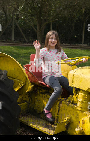Ein Modell veröffentlicht junge Mädchen im Alter von 9 spielen und winken mit dem Traktor auf einem offenen Bauernhof in Bedfordshire. Stockfoto