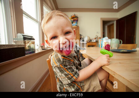 Ein blonder Junge Essen ein Eis am Stiel mit einem unordentlichen Gesicht steckt seine Zunge heraus. Stockfoto