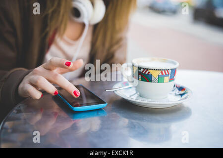 Nahaufnahme von Frau Hand mit Smartphone auf ein Café-Bar-Tisch und eine Tasse Kaffee Stockfoto