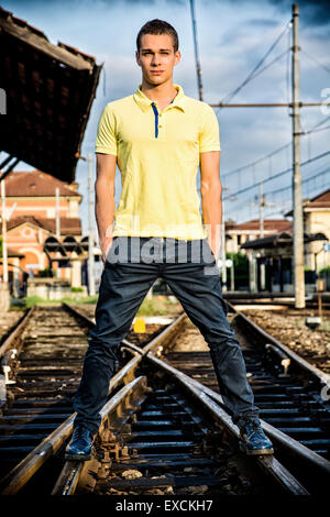 Attraktive junge Mann stehend auf Eisenbahn, tragen gelbe Polo-Shirt und Jeans, Blick in die Kamera Stockfoto