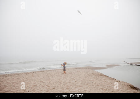 Ein vier Jahre alter Junge spielt auf einem Sandstrand am Lake Michigan an einem nebligen Tag. Stockfoto