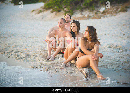 Gruppe von multiethnischen Jugendliche Frauen und Männer am Strand im Sommer sitzen Sand Sonnenuntergang Stockfoto
