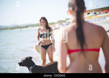 zwei schöne junge Frauen spielen mit Hund am Strand im Sommer Stockfoto