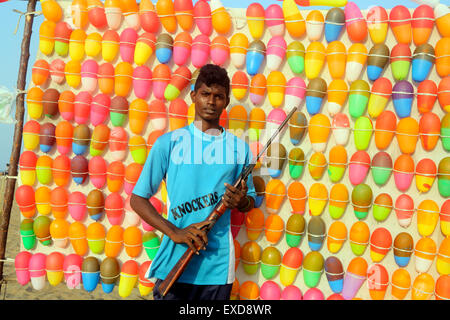 Junge indische Mann hält Luftgewehr am Strand Spaß stall mit Ballon-Ziele Stockfoto