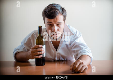 betrunkener junge stilvolle Mann mit weißem Hemd hinter dem Tisch Stockfoto