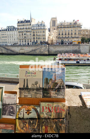 Bücher bei Bouquinistes entlang der Seine mit einem vorbeifahrenden Touristen Kahn, Boot, Paris, Ile De La Cité, Frankreich. Stockfoto