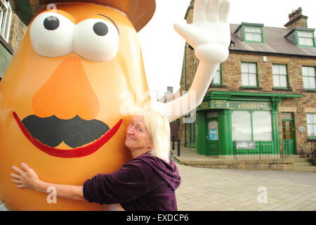 Belper, Derbyshire, UK. 12. Juli 2015. Spud Fan umarmt Freda Raphael eine riesige Mr. Potato Head, das neu erschienen ist in einer Stadt in Derbyshire. Die 7ft hohen Fiberglas-Statue wurde Belper im Jahr 2001 von seiner Partnerstadt, Pawtucket, Rhode Island, USA begabt. Nach wird ein "Monstrum" von einigen Einheimischen genannt, machte die trennende Charakter landesweit Schlagzeilen. Es war verwüstet und verbannt. Jetzt wurde die Knolle von einer lokalen Jugendgruppe herausgeputzt und enthüllt Belpers Food Festival heute. Bildnachweis: Deborah Vernon/Alamy Live-Nachrichten Stockfoto