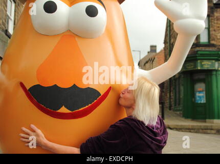 Belper, Derbyshire, UK. 12. Juli 2015. Spud-Fan, Freda Raphael pflanzt einen Kuss auf eine riesige Mr. Potato Head, die neu in einer Stadt Derbyshire erschienen ist. Die 7ft hohen Fiberglas-Statue wurde Belper im Jahr 2001 von seiner Partnerstadt, Pawtucket, Rhode Island, USA begabt. Nach wird ein "Monstrum" von einigen Einheimischen genannt, machte die trennende Charakter landesweit Schlagzeilen. Es war verwüstet und verbannt. Jetzt wurde die Knolle von einer lokalen Jugendgruppe herausgeputzt und enthüllt Belpers Food Festival heute. Bildnachweis: Deborah Vernon/Alamy Live-Nachrichten Stockfoto