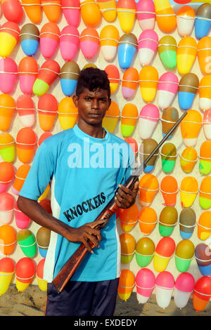 Junge indische Mann hält Luftgewehr am Strand Spaß stall mit Ballon-Ziele Stockfoto