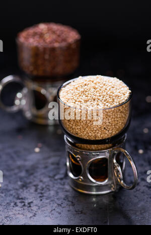 Weiße rohen Quinoa in ein Glas Tasse, rote Quinoa auf Rücken, dunkler Hintergrund, selektiven Fokus Stockfoto