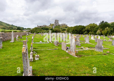 Weit entfernt von der Spitze des Hügels Ruinen des 11. Jahrhunderts Norman Corfe Castle mit einem alten Friedhof mit Grabsteinen im Vordergrund gefüllt. Stürmischen Himmel. Stockfoto