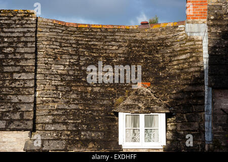Englisches Dorf, Corfe. Details von unebenen Schiefer Dach einer alten Hütte Haus mit Dachfenster und modernen Kamin. Stürmische grauer Himmel Hintergrund. Stockfoto