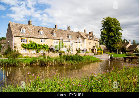 Ansichtskarte Blick auf die Reihe der Cotswold Cottage terrasse Häuser mit den langsam fließenden Fluss Auge im Vordergrund Lower Slaughter. Blue Sky. Stockfoto