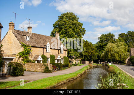 Ansichtskarte Blick auf die Reihe der Cotswold Cottage terrasse Häuser mit den langsam fließenden Fluss Auge im Vordergrund Lower Slaughter. Blue Sky. Stockfoto