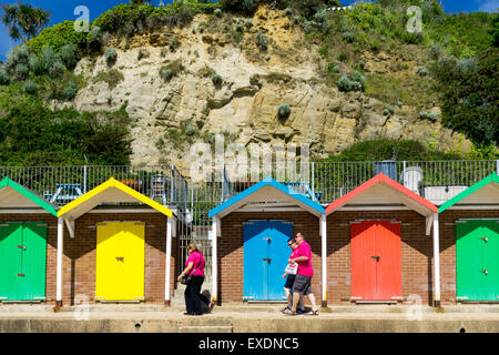 Menschen zu Fuß vorbei an bunt bemalten Strandhütten in Swanage, Dorset, Großbritannien Stockfoto