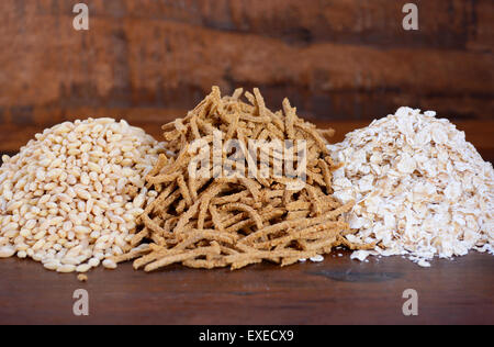 Stapel von gesunden hohe Faser Präbiotikum Körner einschließlich Weizen-Kleie-Müsli, Haferflocken und Graupen auf rustikalen dunklen Holztisch Stockfoto