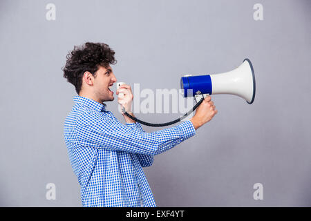 Legerer Mann schreien über Megaphon auf grauem Hintergrund Stockfoto