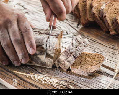 Die Hände des Mannes schneiden Roggenbrot auf das Holzbrett. Stockfoto