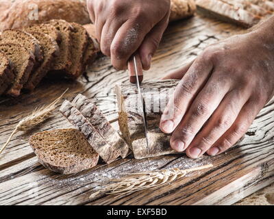 Die Hände des Mannes Schneiden von Brot auf das Holzbrett. Stockfoto