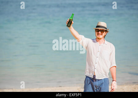 Mann mit Hut und Sonnenbrille Enjoing Bier in der Flasche am Strand Stockfoto