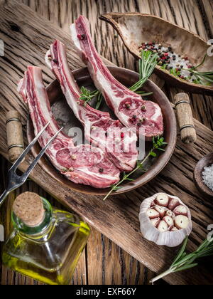 Rohe Lammkoteletts mit Knoblauch und Kräutern auf dem alten Holztisch. Stockfoto