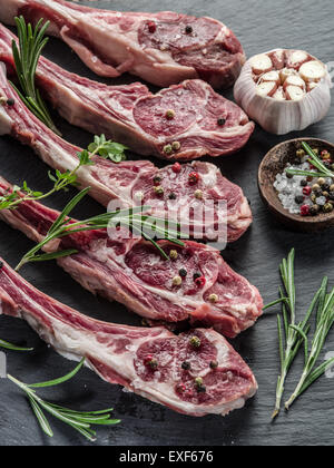 Rohe Lammkoteletts mit Knoblauch und Kräutern auf dem alten Holztisch. Stockfoto